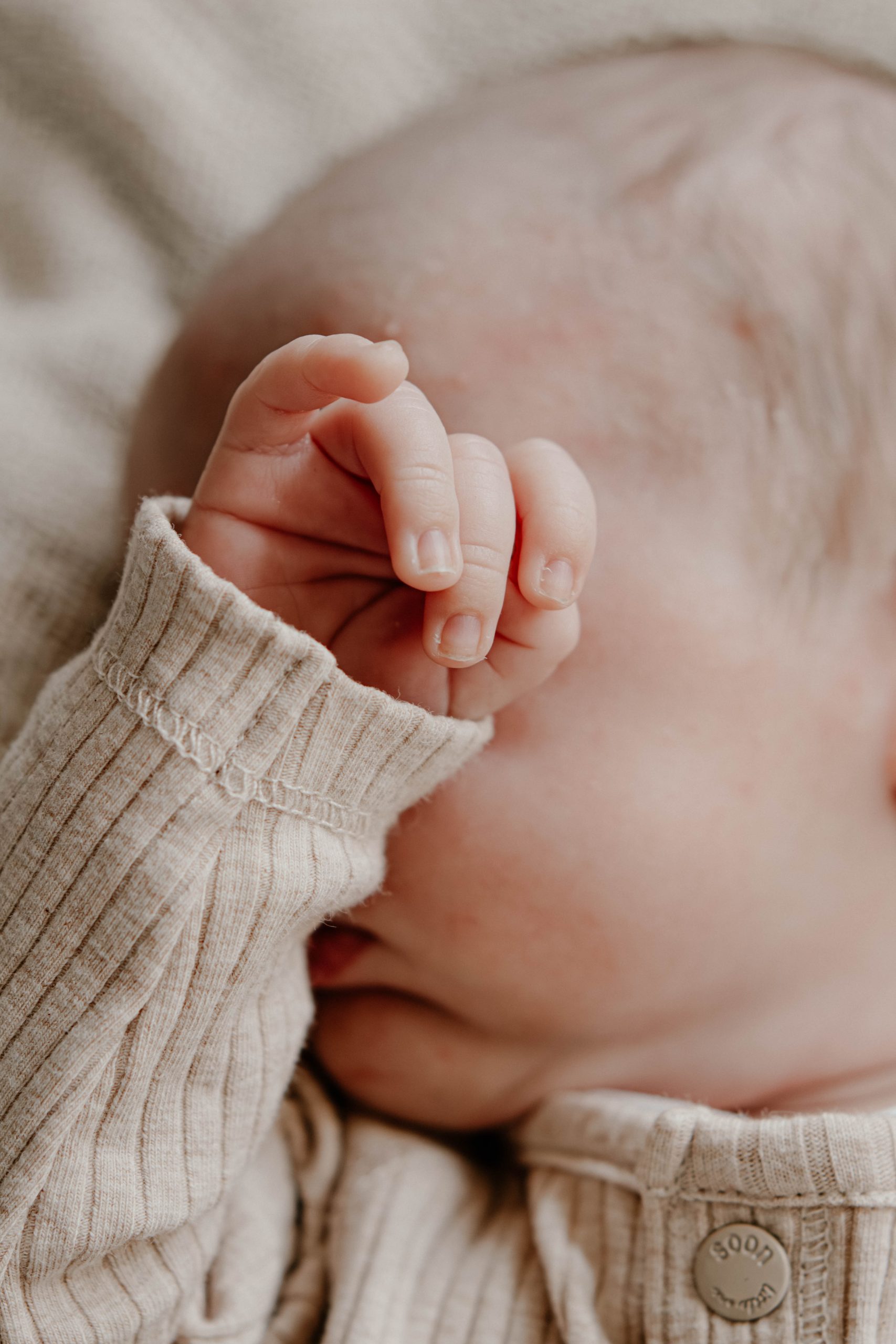 Pasgeboren baby met een handje over het gezicht, passend bij het thema rust en bescherming na de bevalling