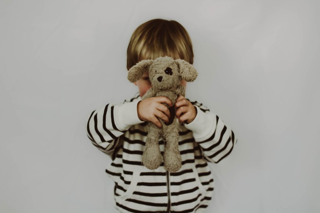Kind met knuffel voor het gezicht terwijl moeder worstelt met onvervulde kinderwens voor een tweede kind