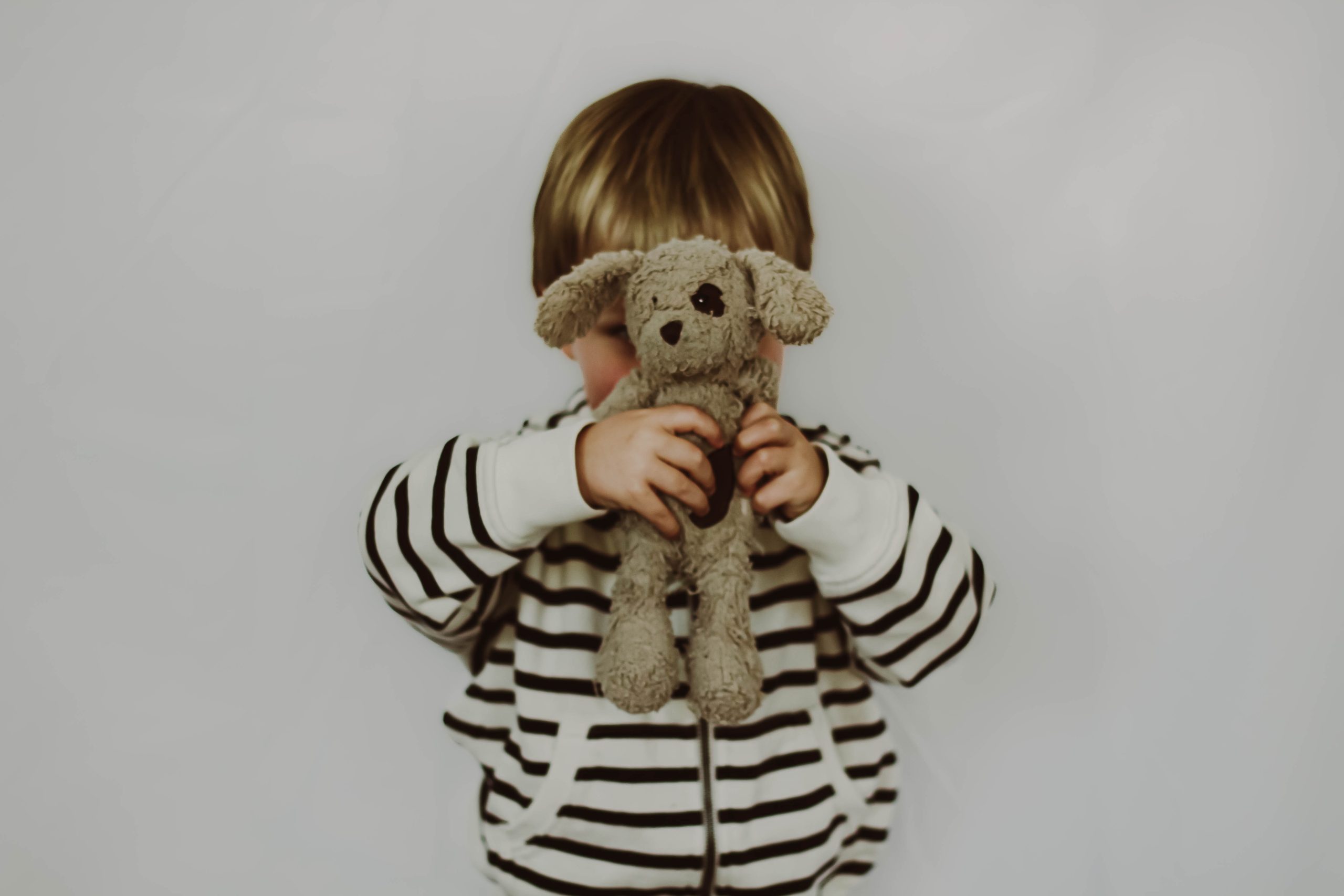 Kind met knuffel voor het gezicht terwijl moeder worstelt met onvervulde kinderwens voor een tweede kind